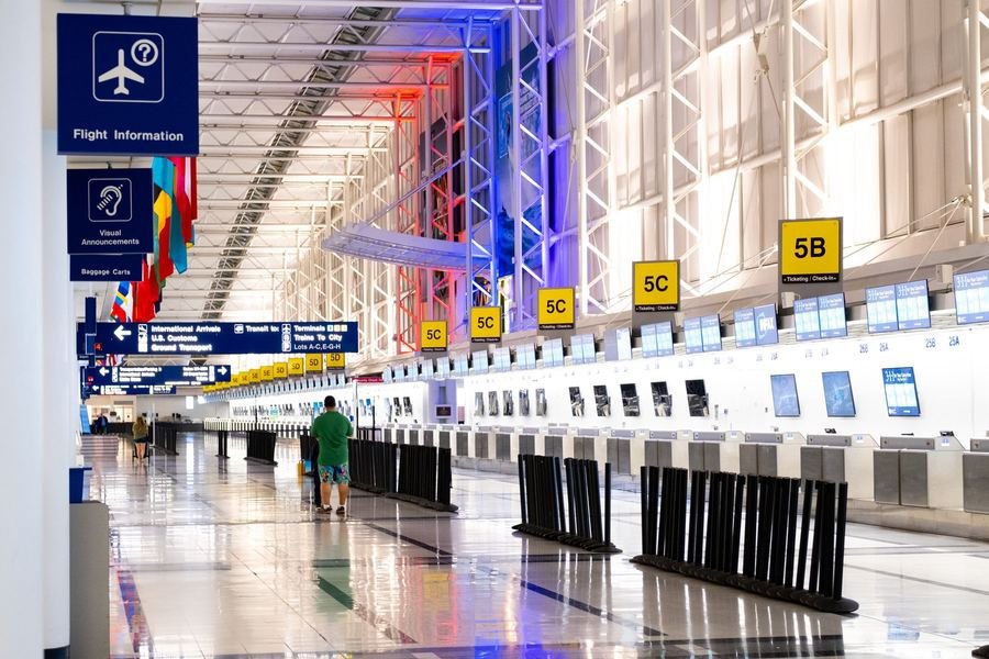 Bright modern airport departures hall with a long row of check-in counters and flight information screens