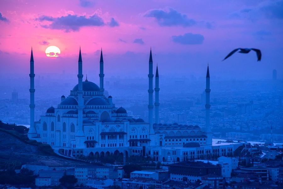 Istanbul skyline at sunset with a large domed mosque and six minarets silhouetted against a pink sky