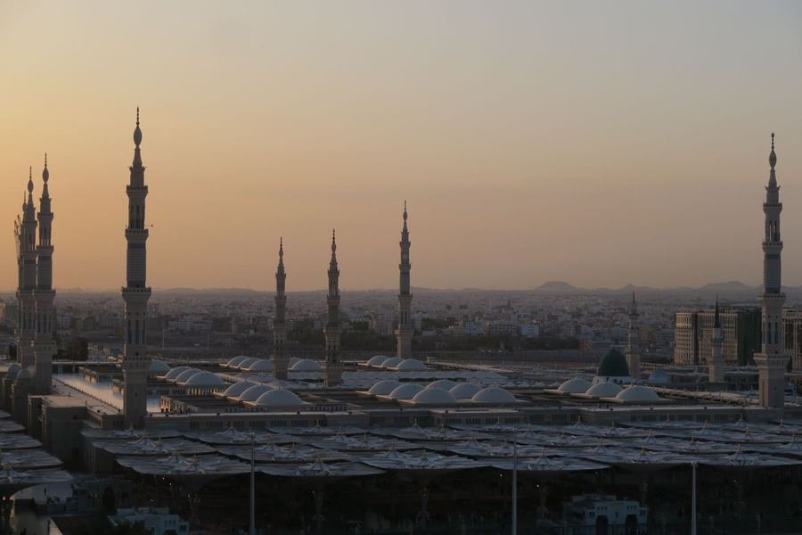 Al-Masjid an-Nabawi in Madinah at sunset with minarets, white roof domes and the green dome