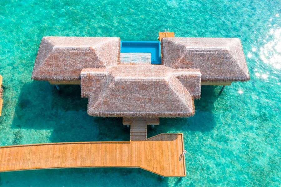 Aerial view of thatched overwater villas and a timber boardwalk on a turquoise Maldives lagoon