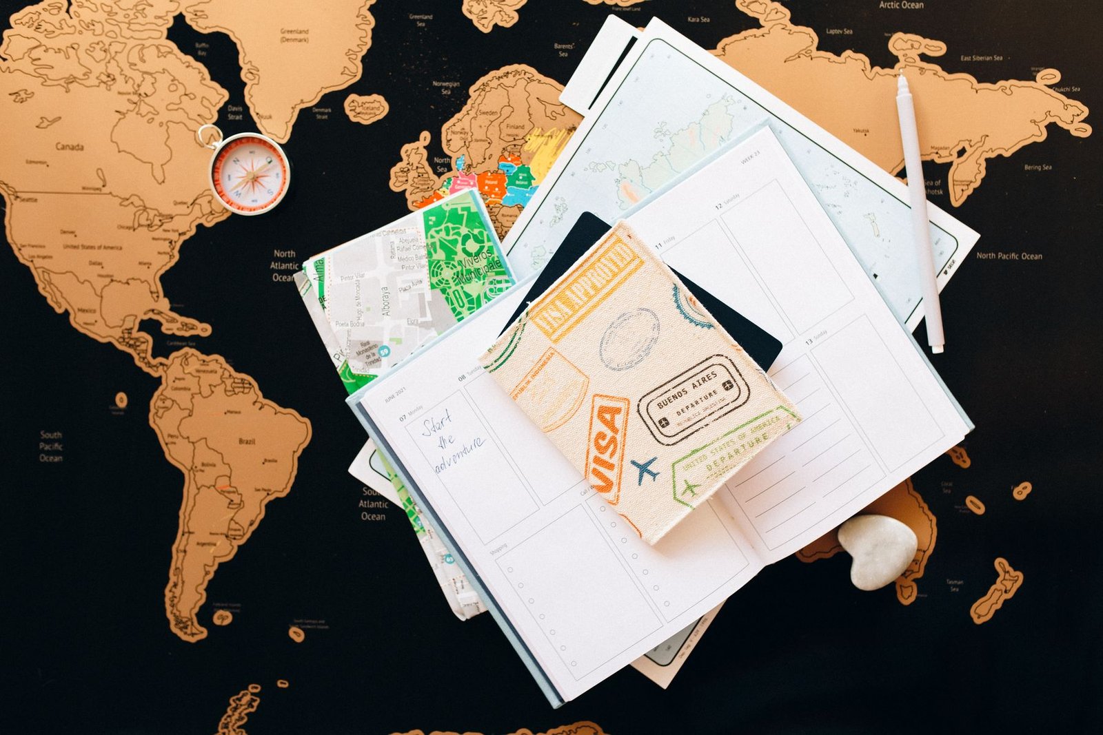 Passport with entry stamps, a travel planner, folded maps and a compass laid out on a world map for a visa application